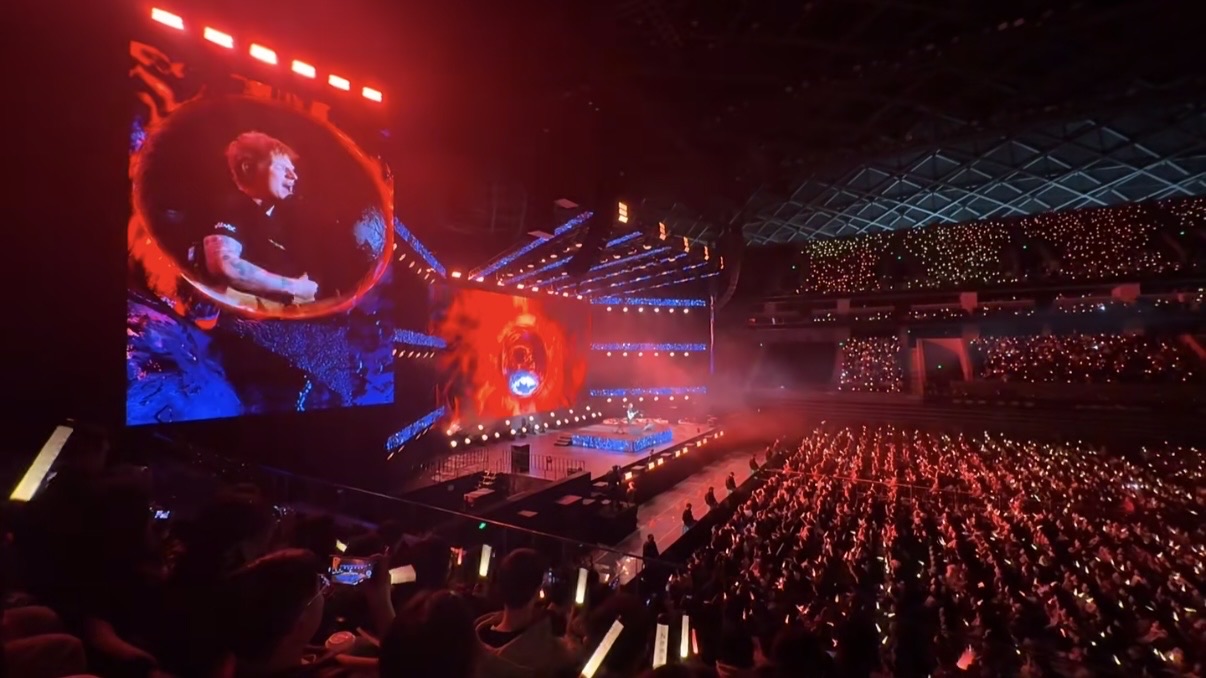 Concert crowd in front of a large touring LED screen at night